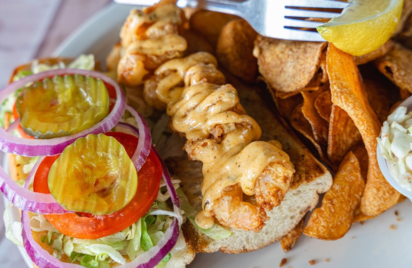 Closeup of a Po' Boy shrimp sandwich with some chips on the side