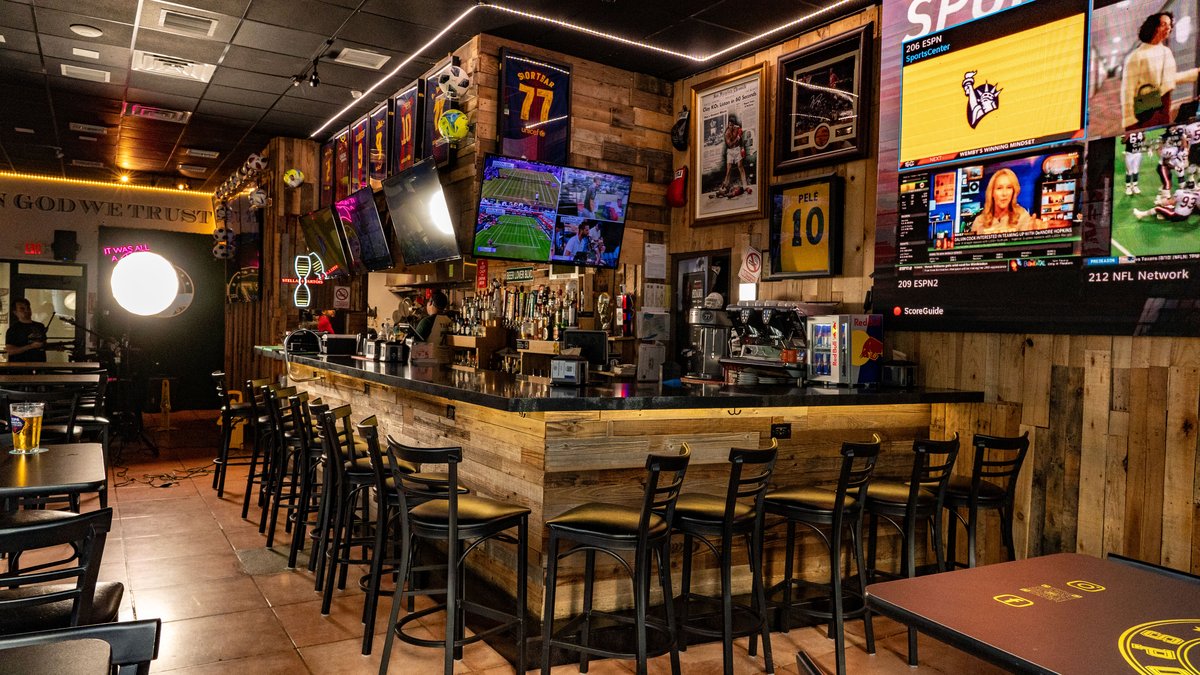 A bar with several televisions and stools.