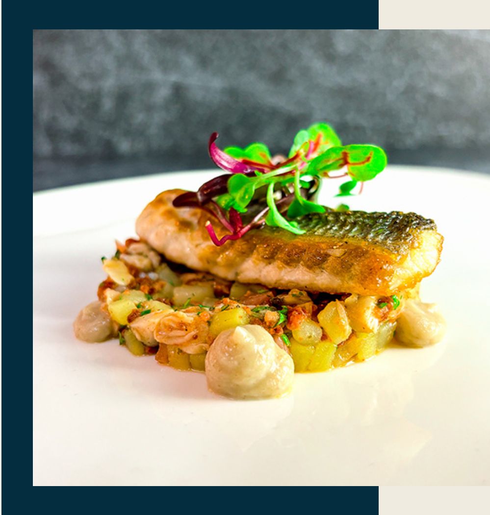 A seared fish fillet served on a bed of diced vegetables, garnished with microgreens.