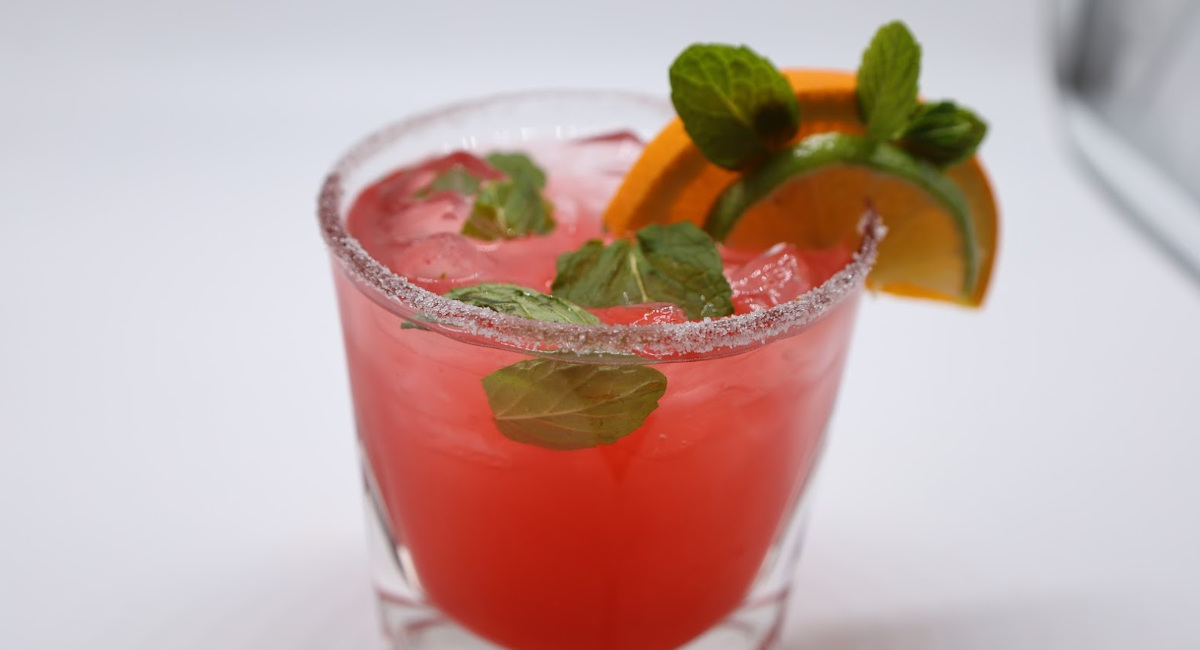 Red cocktail drink garnished with lime and orange wedges and mint leaves