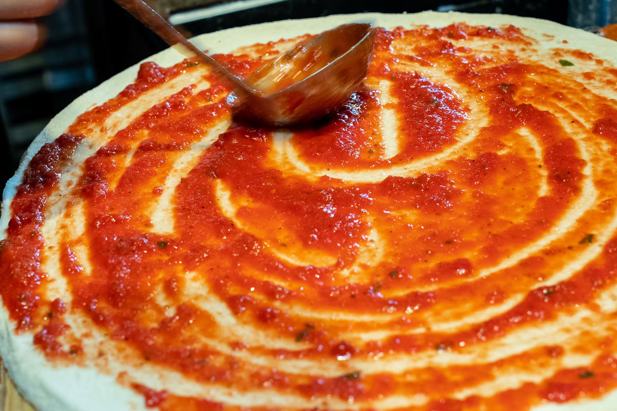Spreading tomato sauce on pizza using ladle