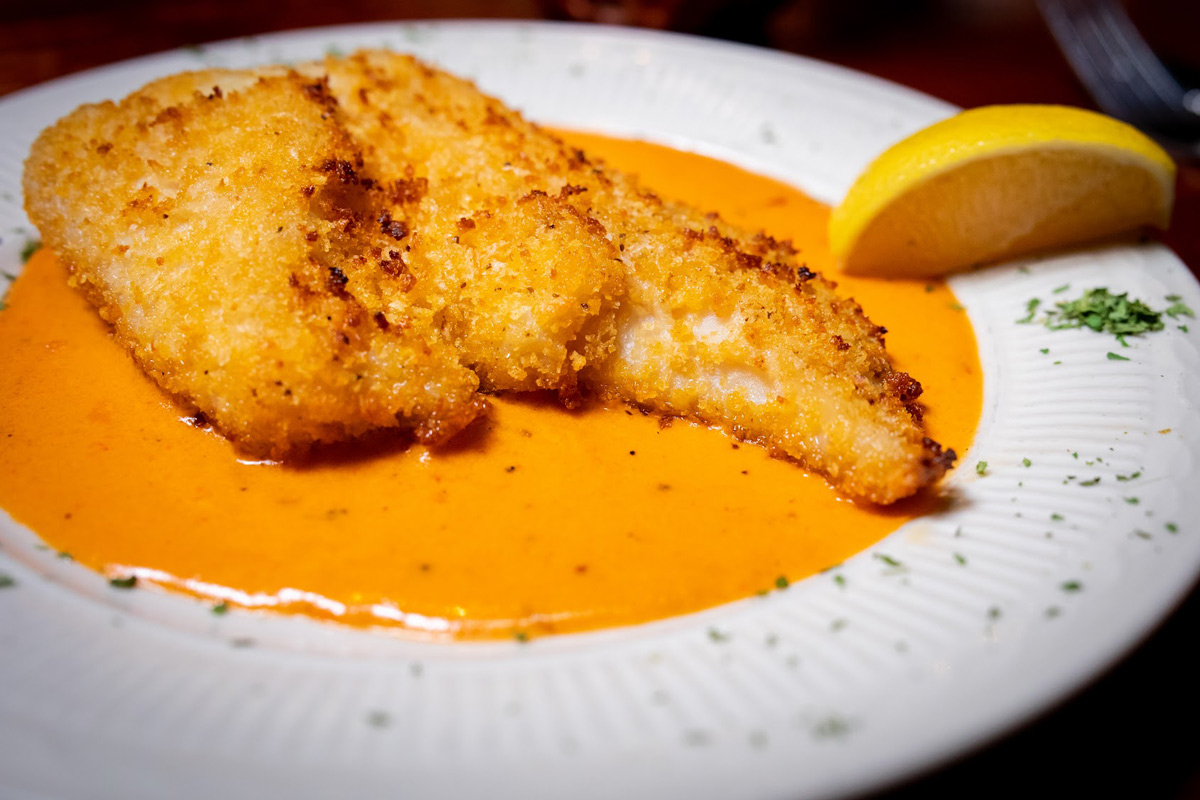 Deep fried salmon filet covered with a sauce and a lemon wedge