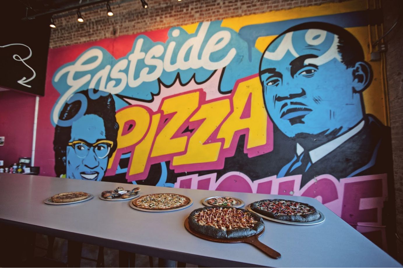 Assorted pizzas on a table, mural art in the background