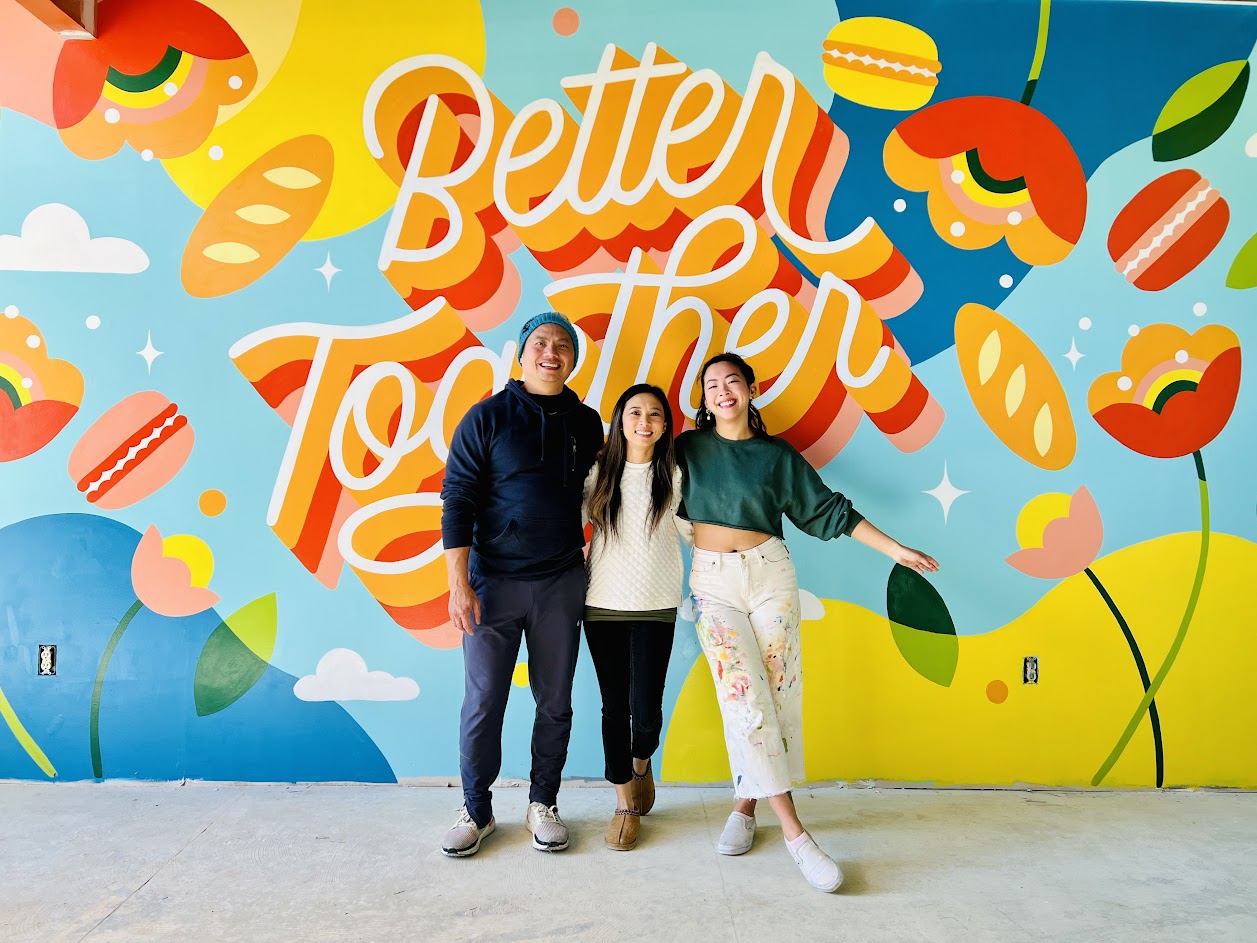 Three people posing for the photo in front of a huge mural art