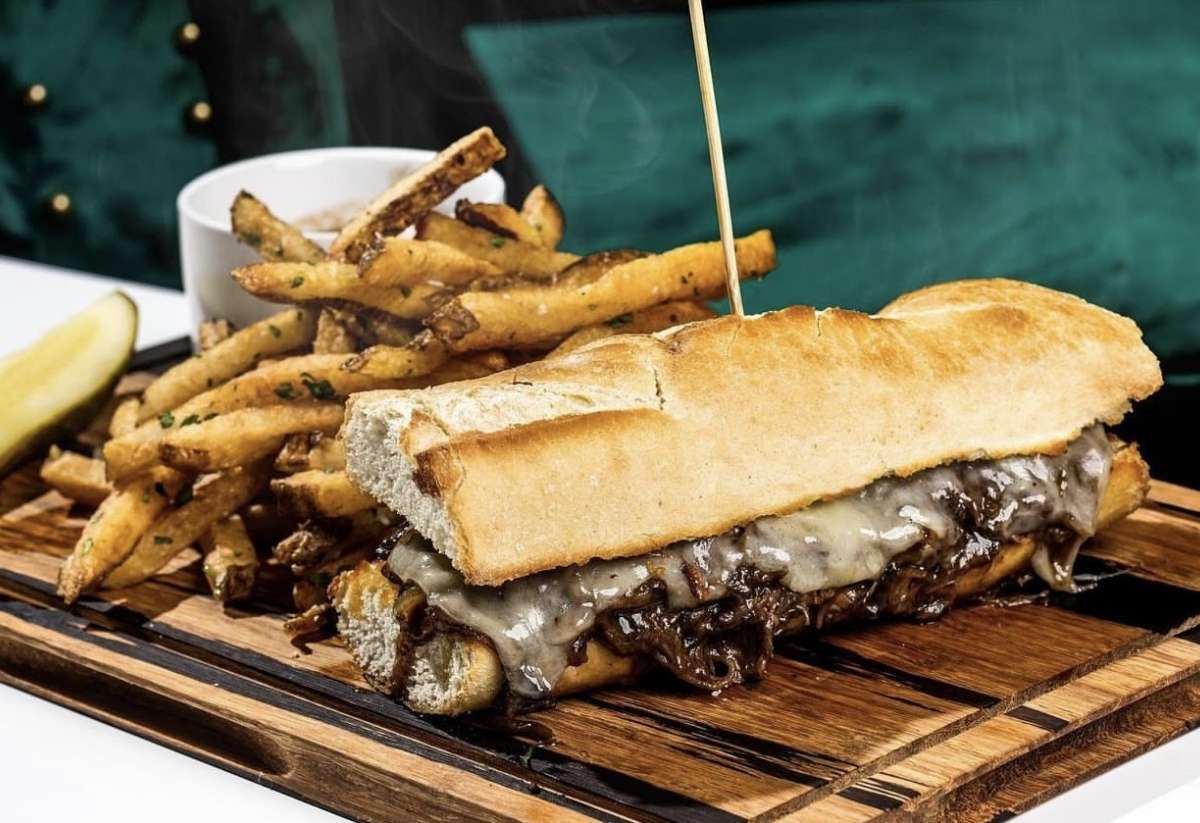 Cheese  steak sandwich served on a board with seasoned fries