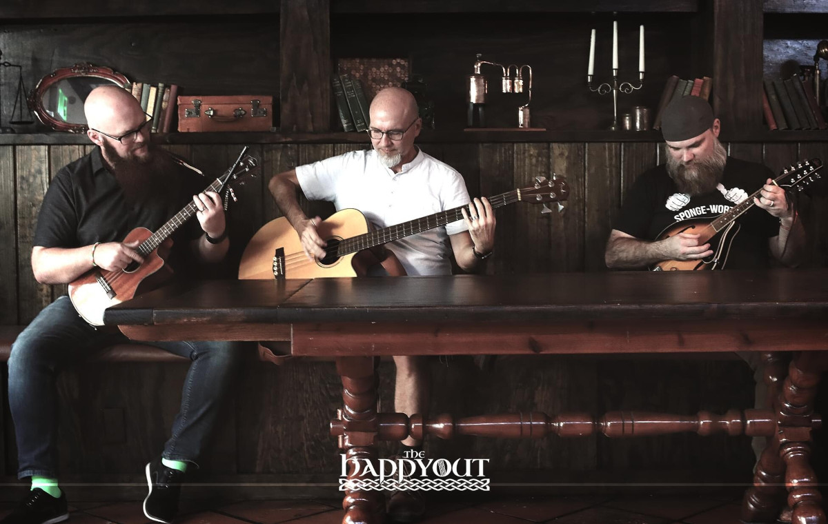 Three men seated at a table, each playing a guitar