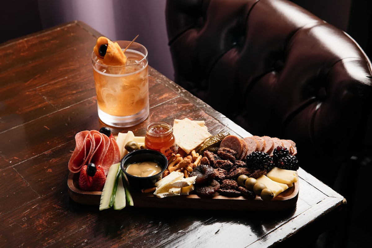 Charcuterie board served on a table with a cocktail drink
