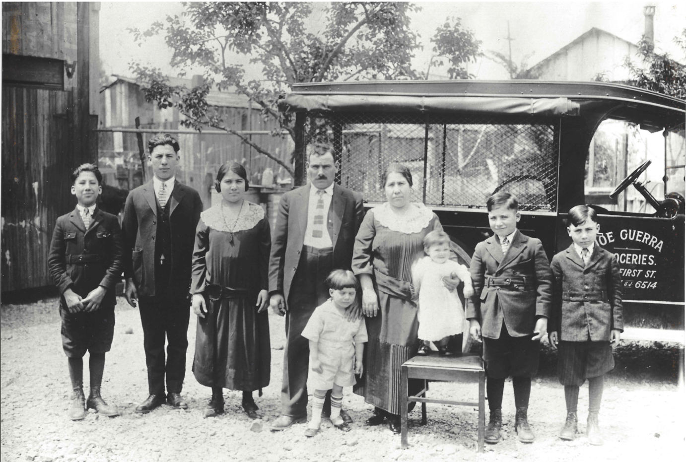 Historical photo of the Guerra family posing outside with groceries vehicle in the back