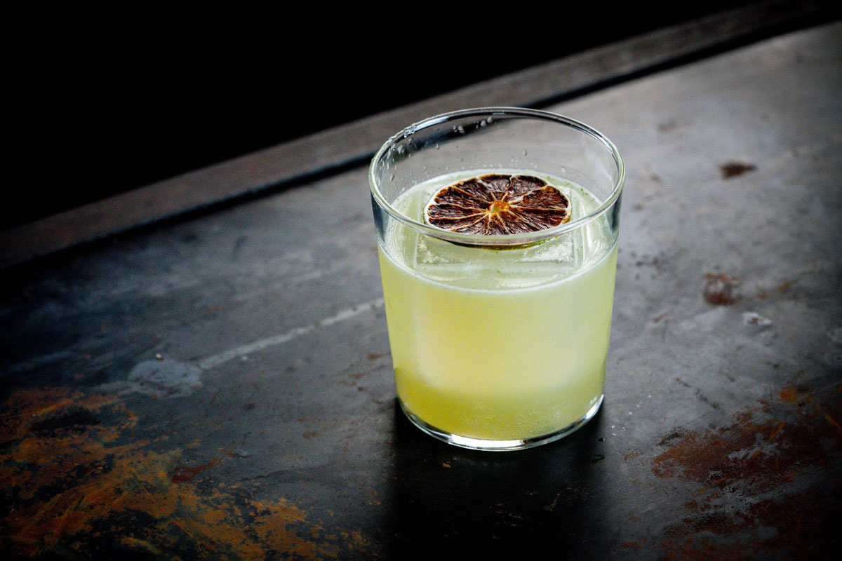 Glass of yellowish cocktail drink garnished with a dried citrus wheel 