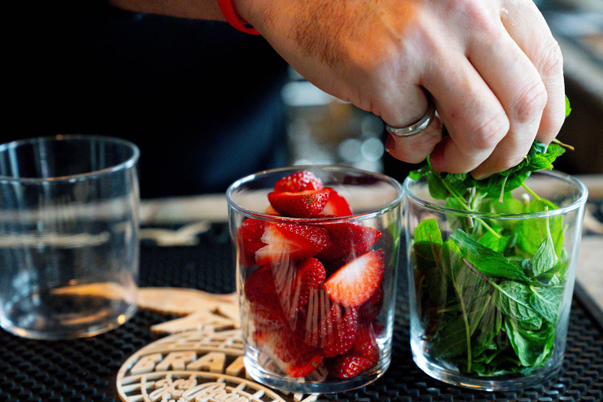 Bartender's hand taking a pinch of mint leaves for cocktail garnish