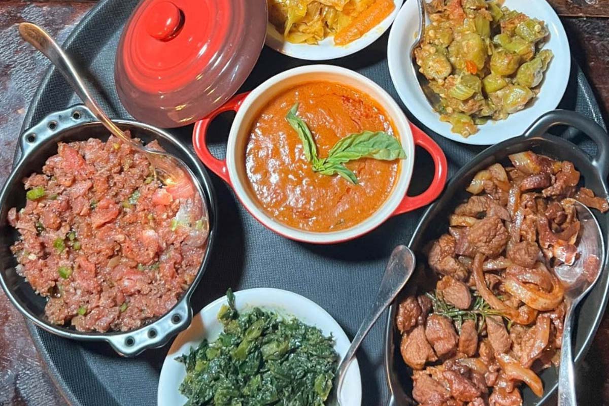 A large platter with stew, beef, and sides of collards, cabbage, and sauteed okra