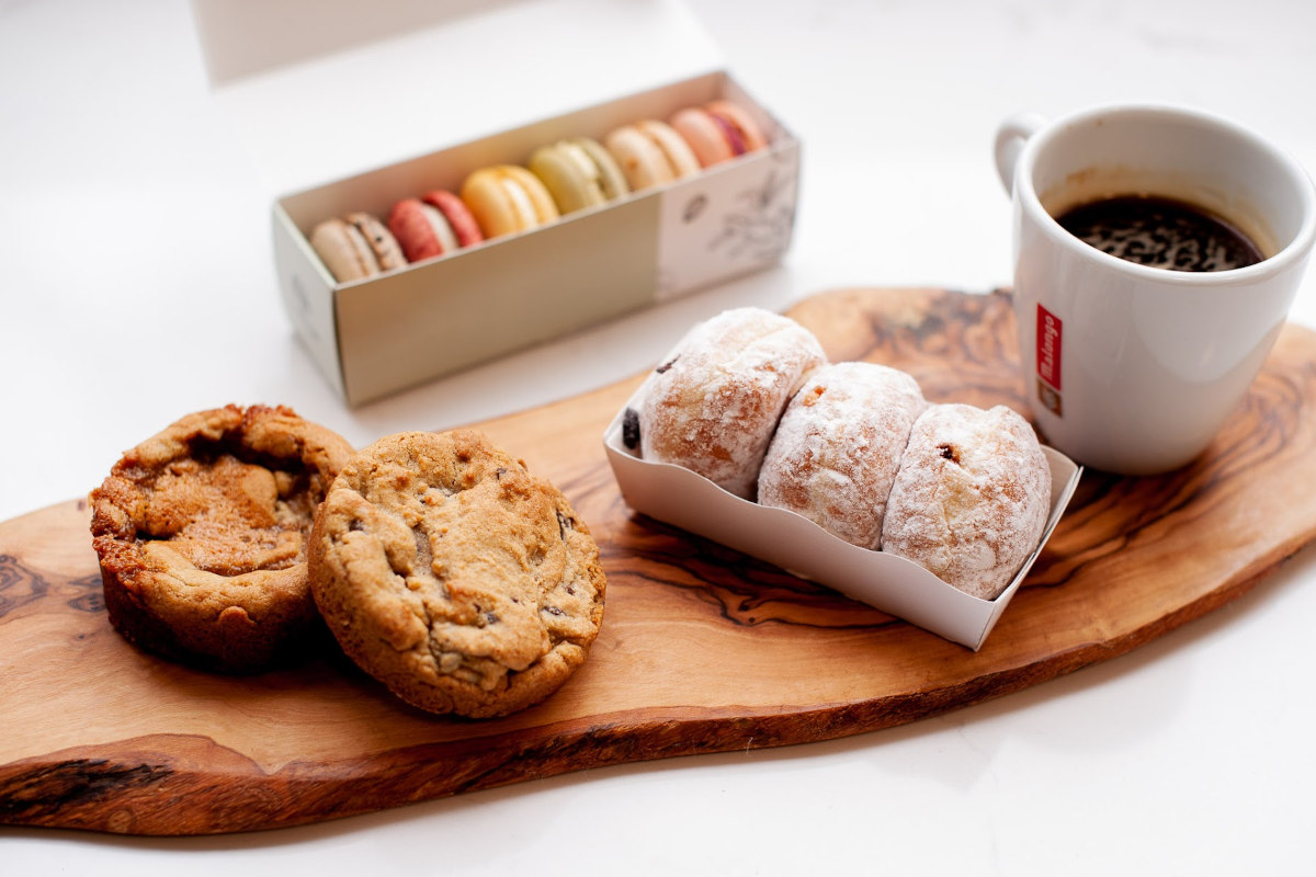 Cookies, donuts and a coffee on a board with a small box of macaroons in the background 