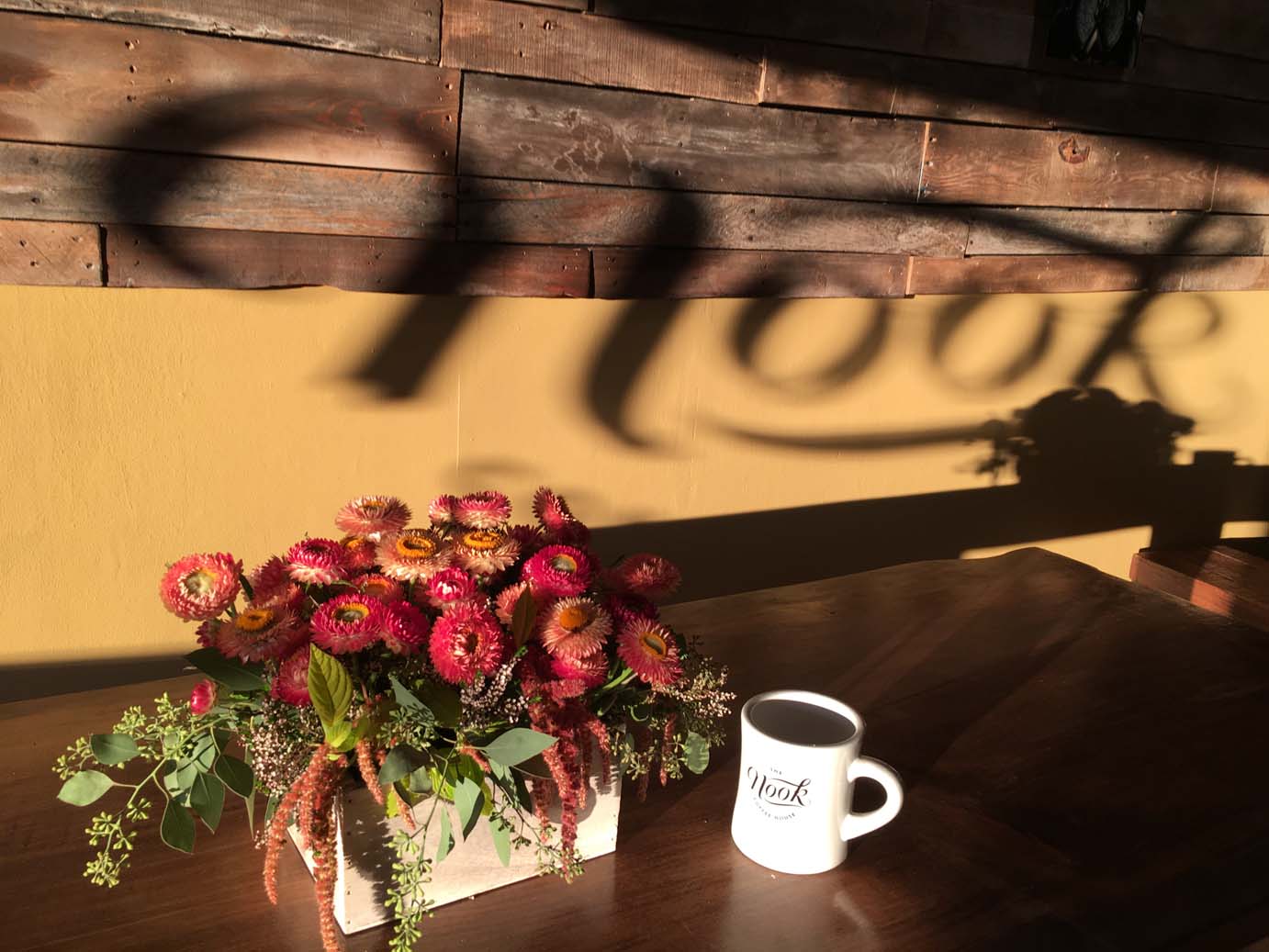 Sun lit flower box and coffee on the table with window shadow  on the wall