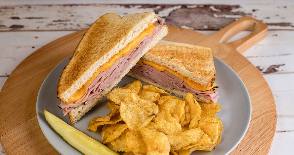 Ham and cheese sandwich served with potato chips and pickle