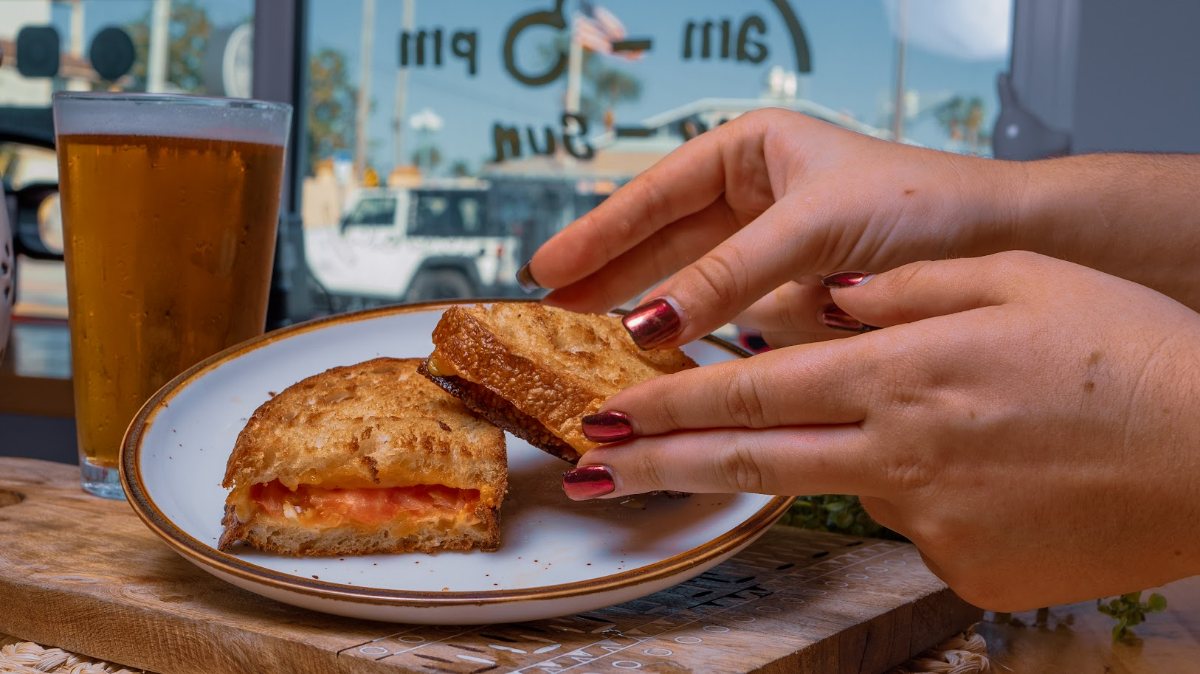 Hands taking grilled cheese sandwich from the plate accompanied with beer