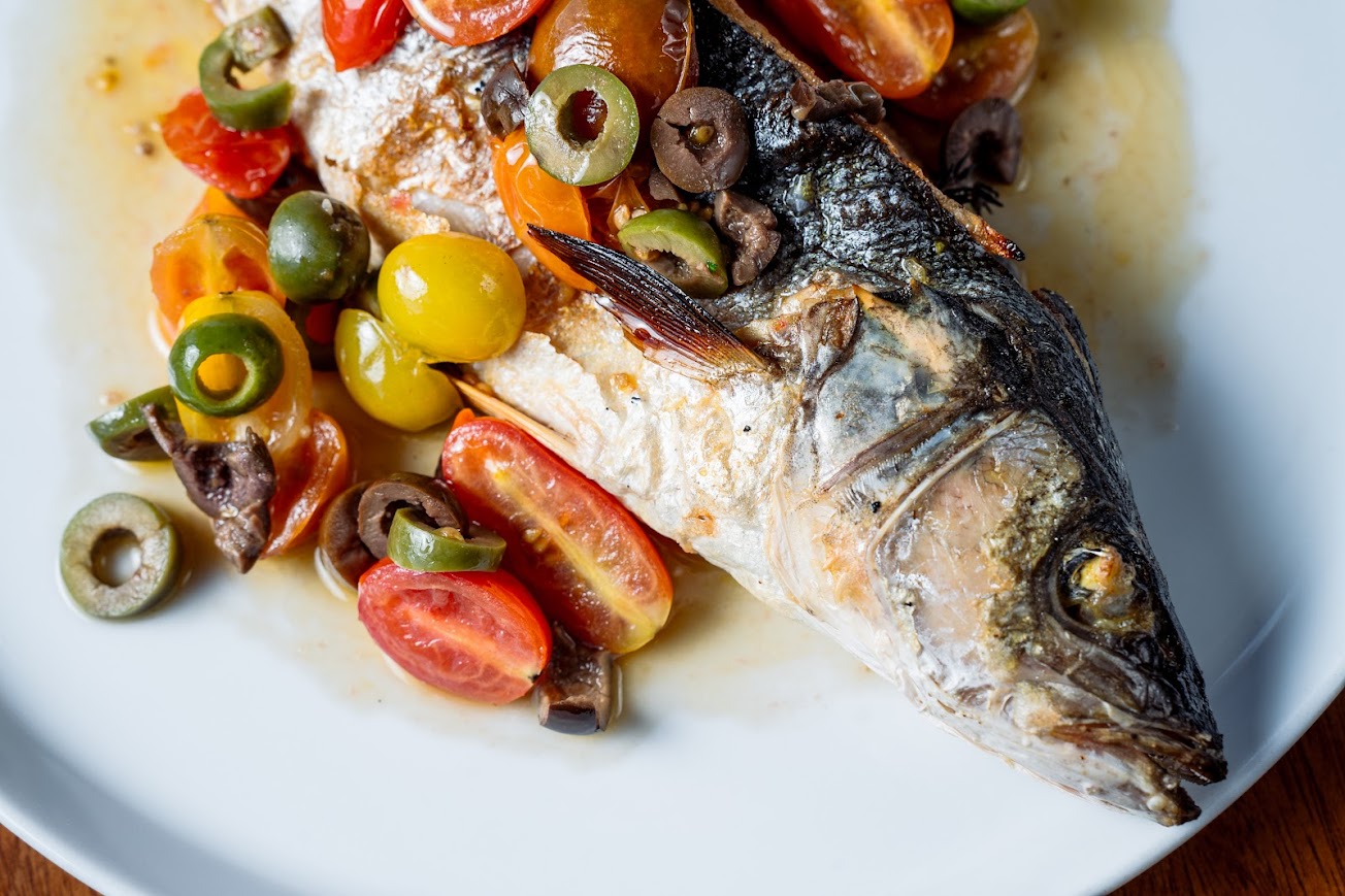 Close up of whole branzino served with cherry tomatoes and olives, top view