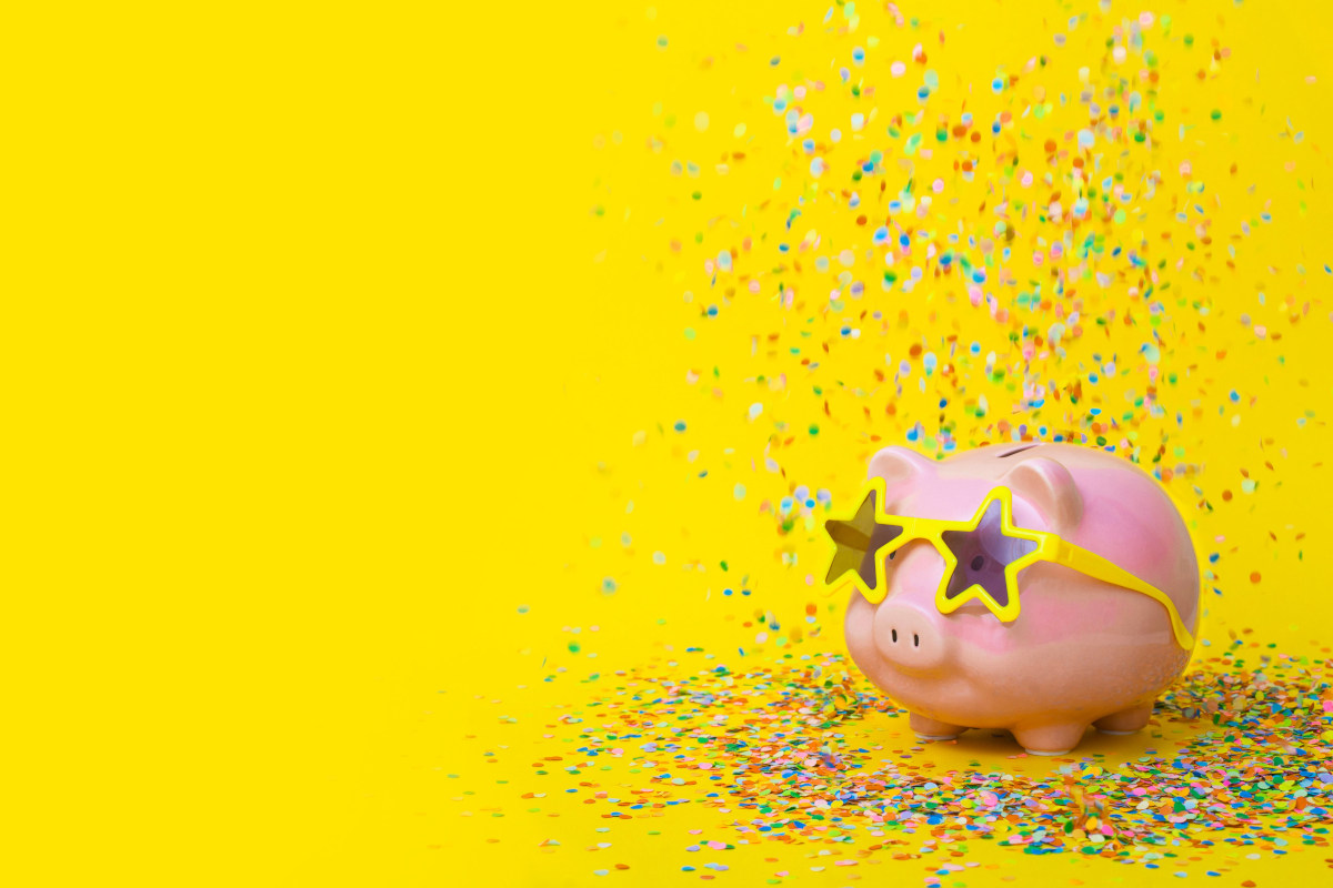 Rainbow sprinkles falling on a pink piggy bank placed against yellow background