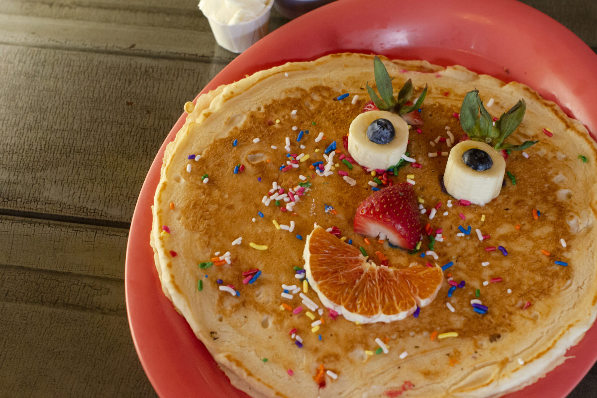 Crepe garnished with rainbow sprinkles and smiley face made of fruit