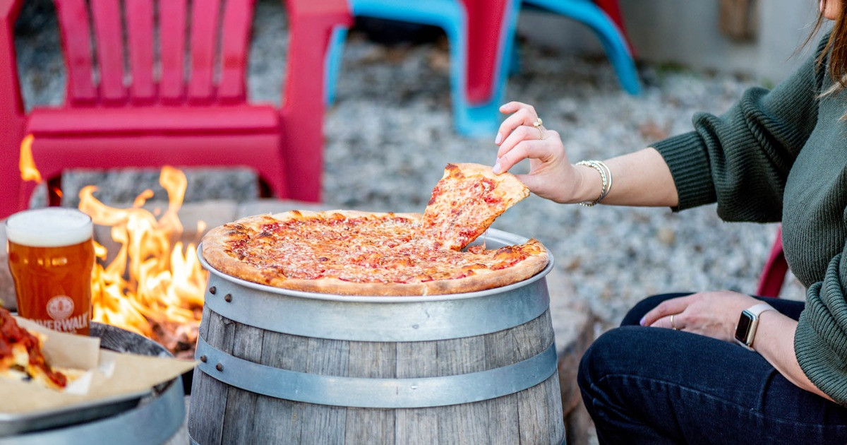 A Woman eating a slice of pizza on a barrel.