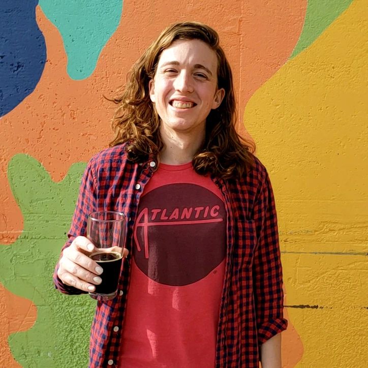 Wylie posing with a beer in front of a mural wall, headshot