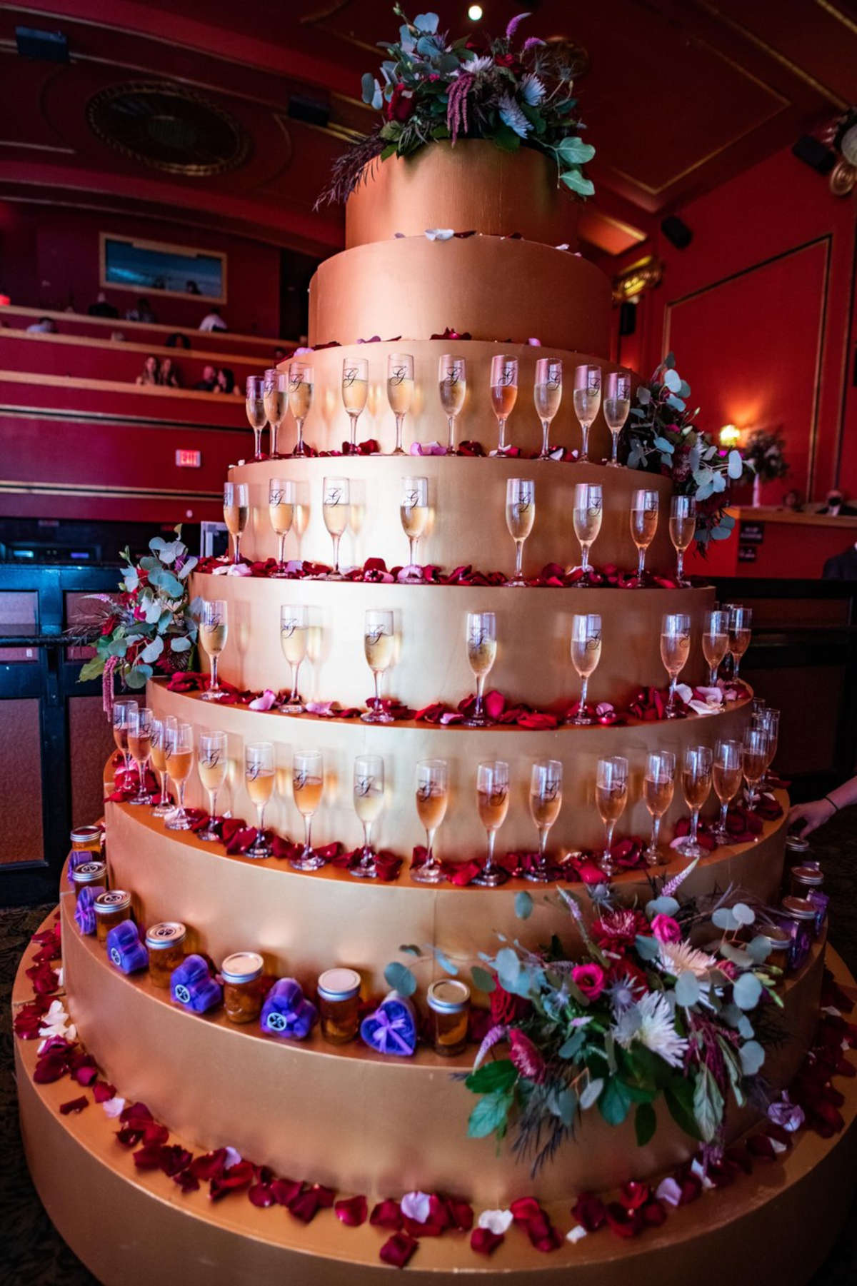 A large multi tiered cake shaped stand with glasses of sparkling wine and floral garnish