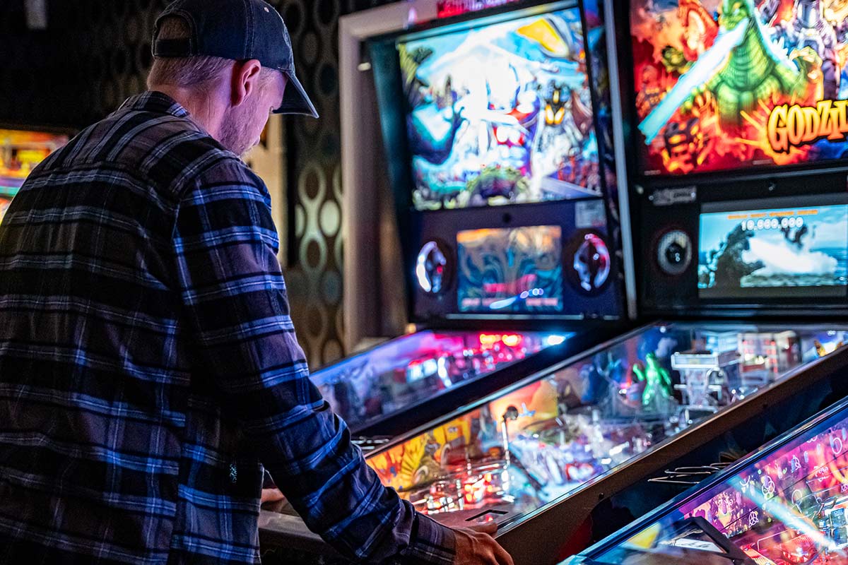 A man engaged in playing a pinball machine within a game room.