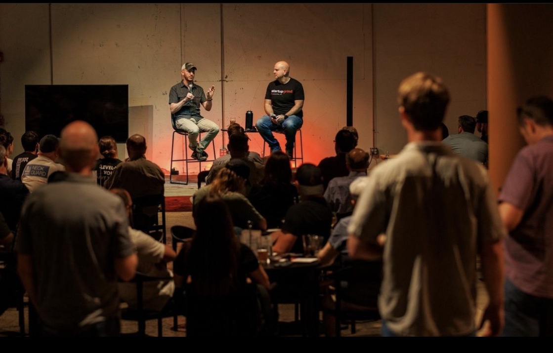 Two men are seated on stage, speaking to a captivated audience in front of them