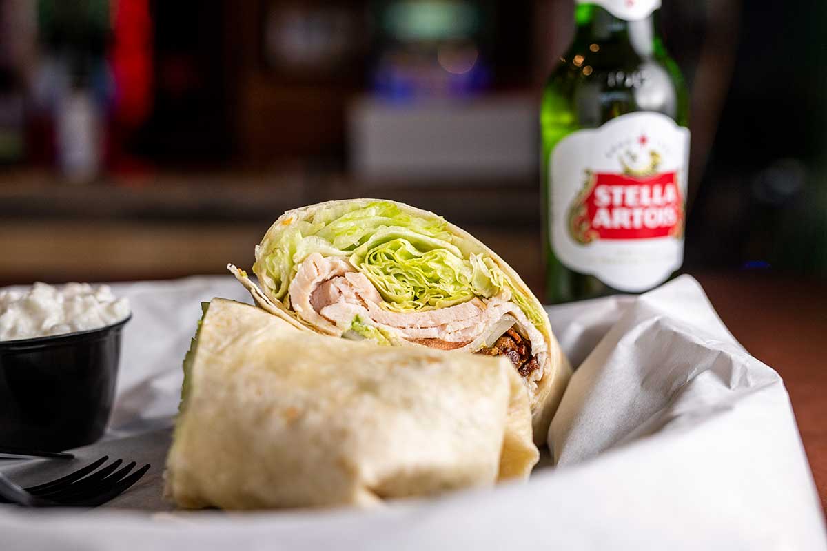 Turkey wrap sandwich with lettuce and dressing, beer bottle on the side