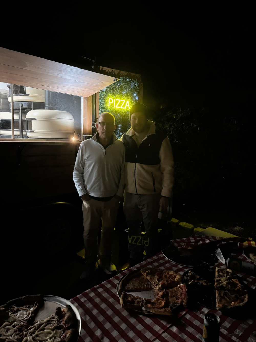 two workers standing next to the pizza truck