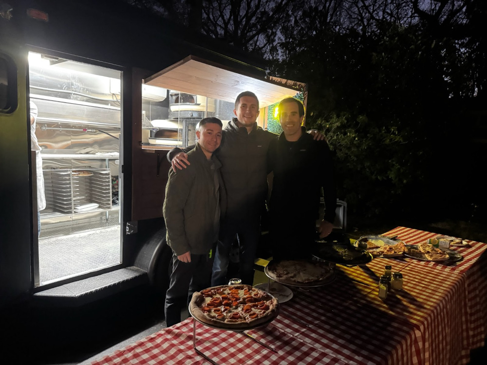 three workers standing next to the pizza truck