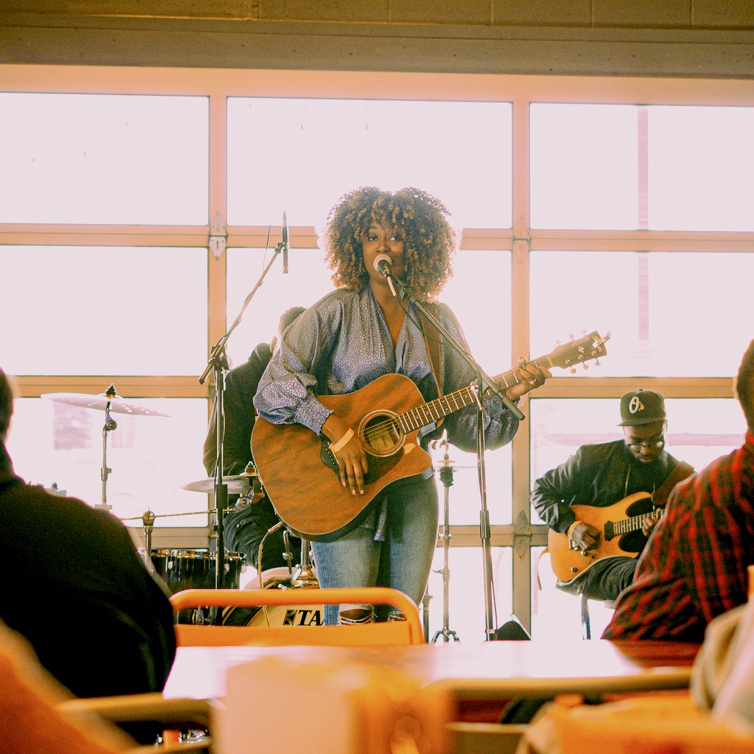 a person singing into a microphone with a guitar in front of a group of people