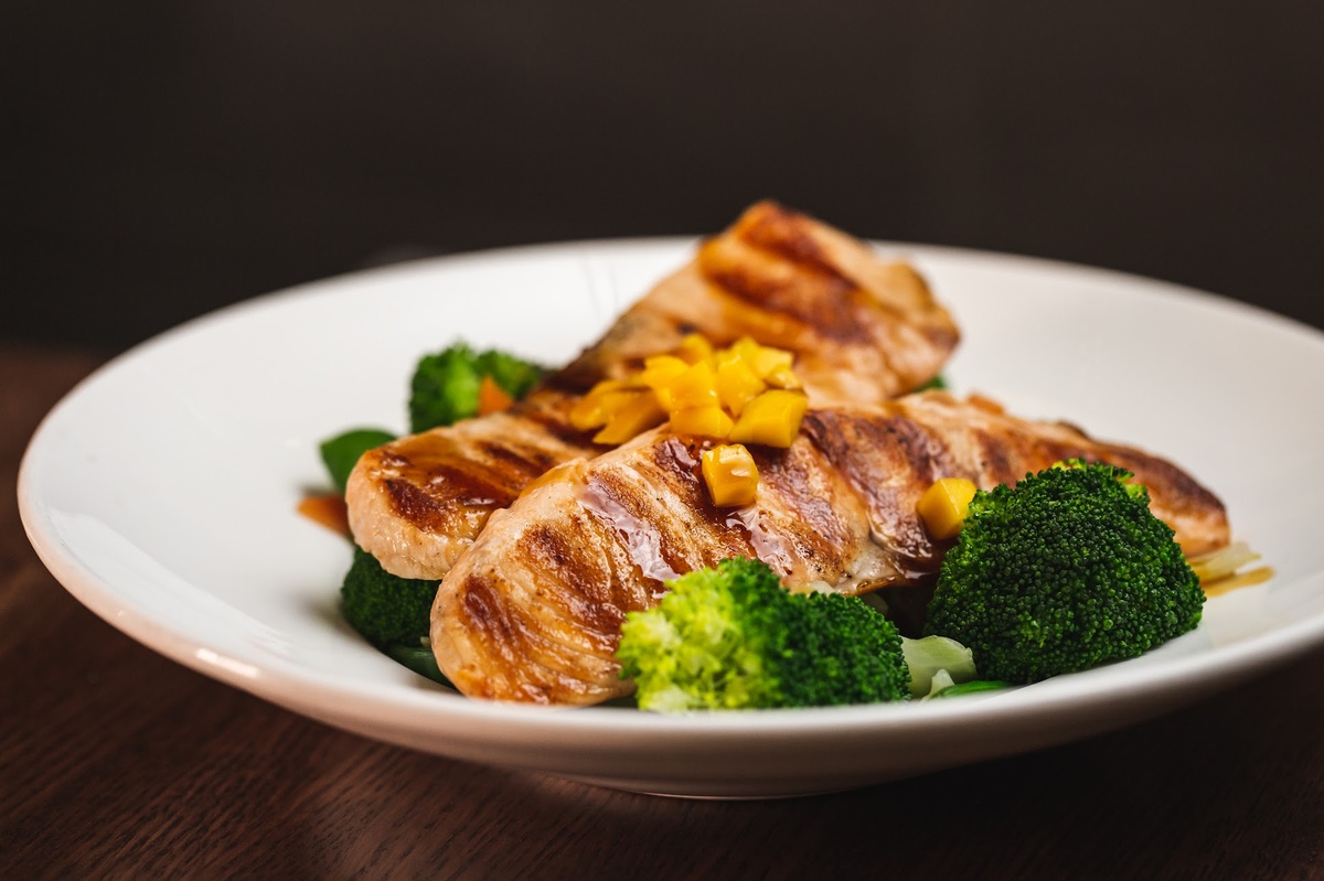 Grilled chicken slices with broccoli and corn on a white plate.