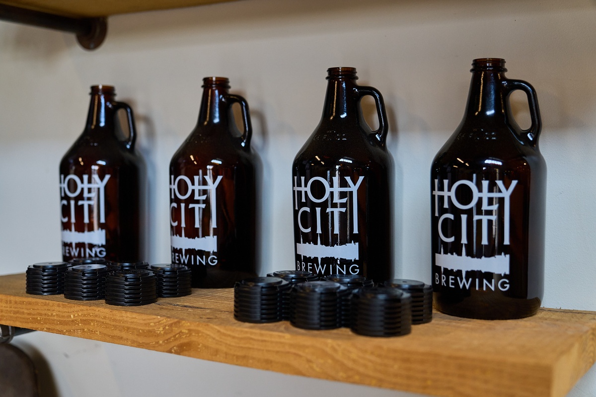 Four dark brown glass growler bottles with white labels reading Holy City Brewing