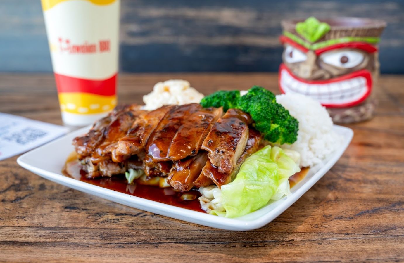 Closeup of a plate of Teriyaki chicken with some lettuce and rice on the side