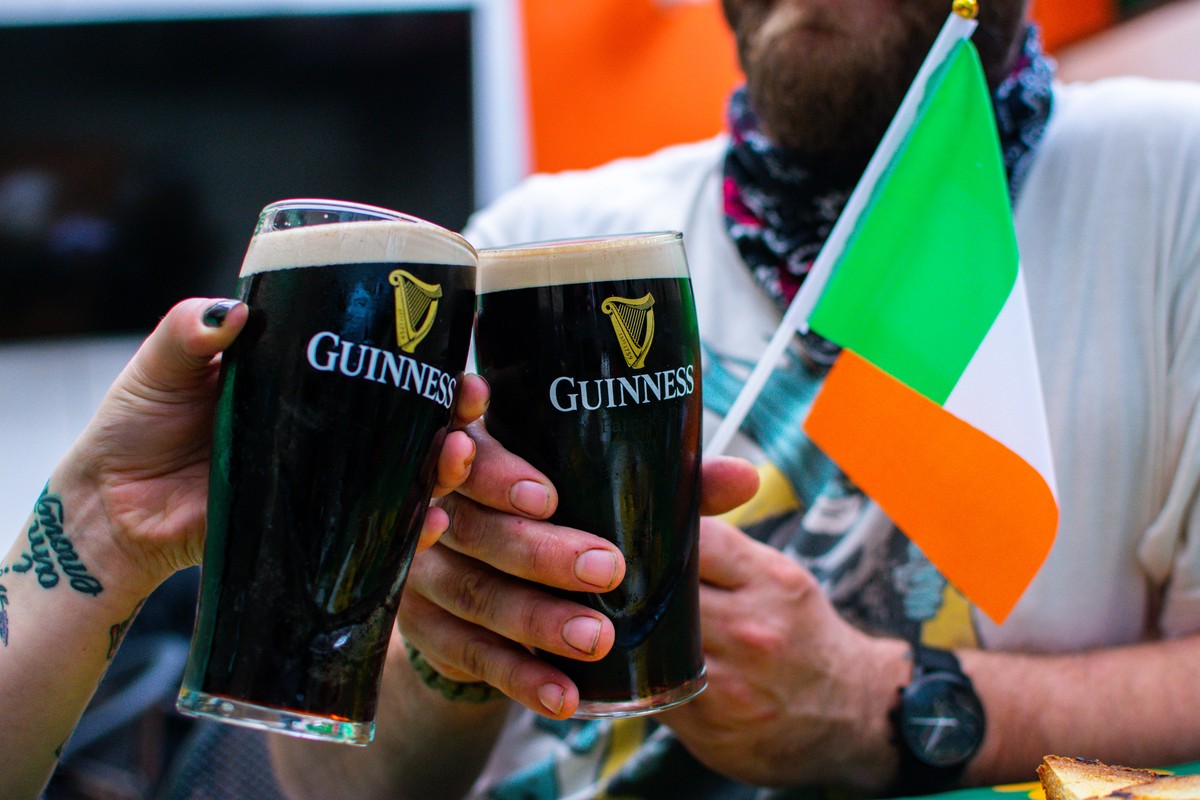 Two people holding guinness pint glasses and an irish flag.