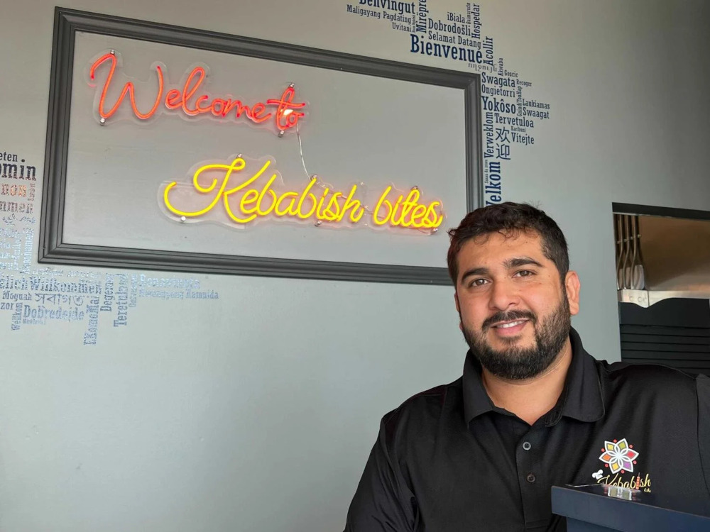 Kebabish Bites owner Waseem Ahmed smiling in front of the restaurant's welcome sign