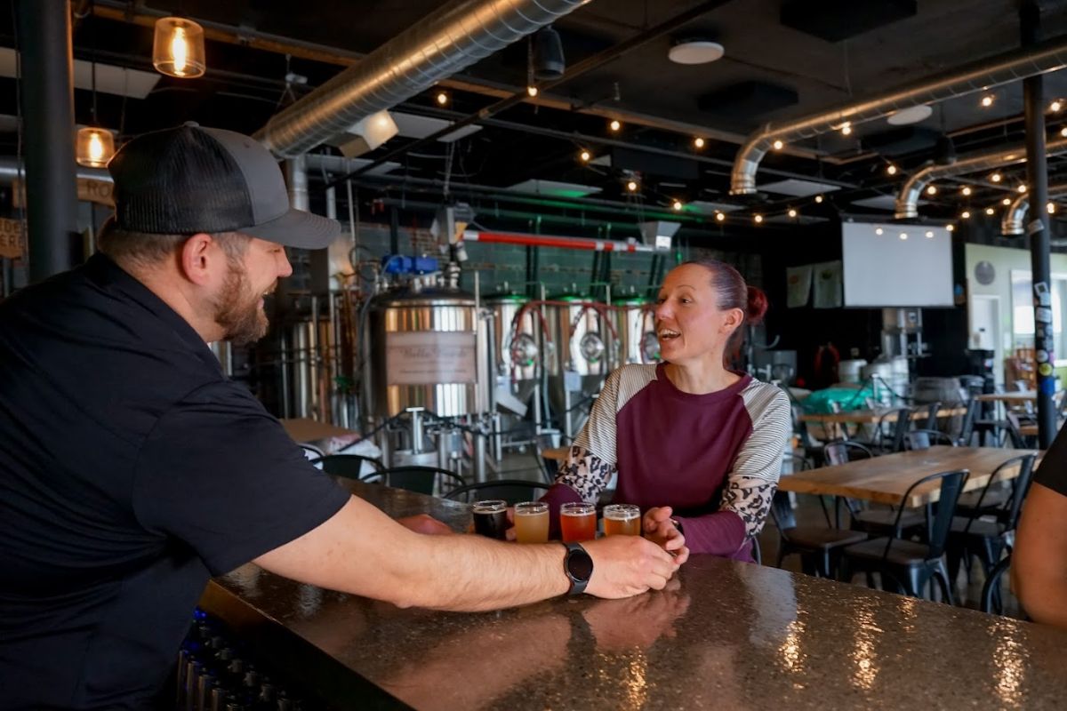 Interior, a bartender serves a beer flight to a customer