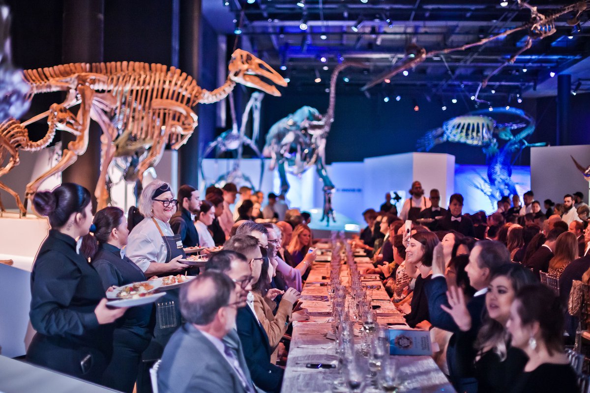 A group of people are sitting at a table in front of dinosaur skeletons