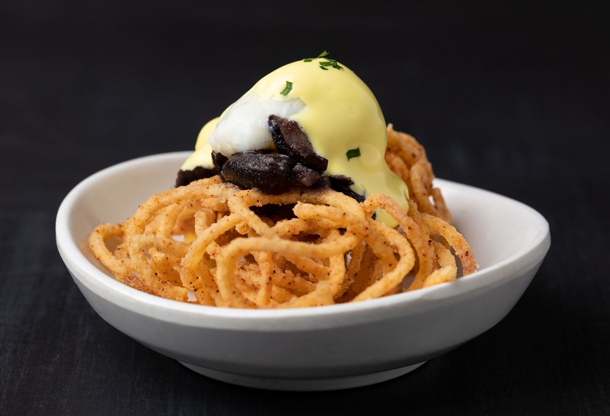 An egg benedict with onion rings and mushrooms in a white bowl