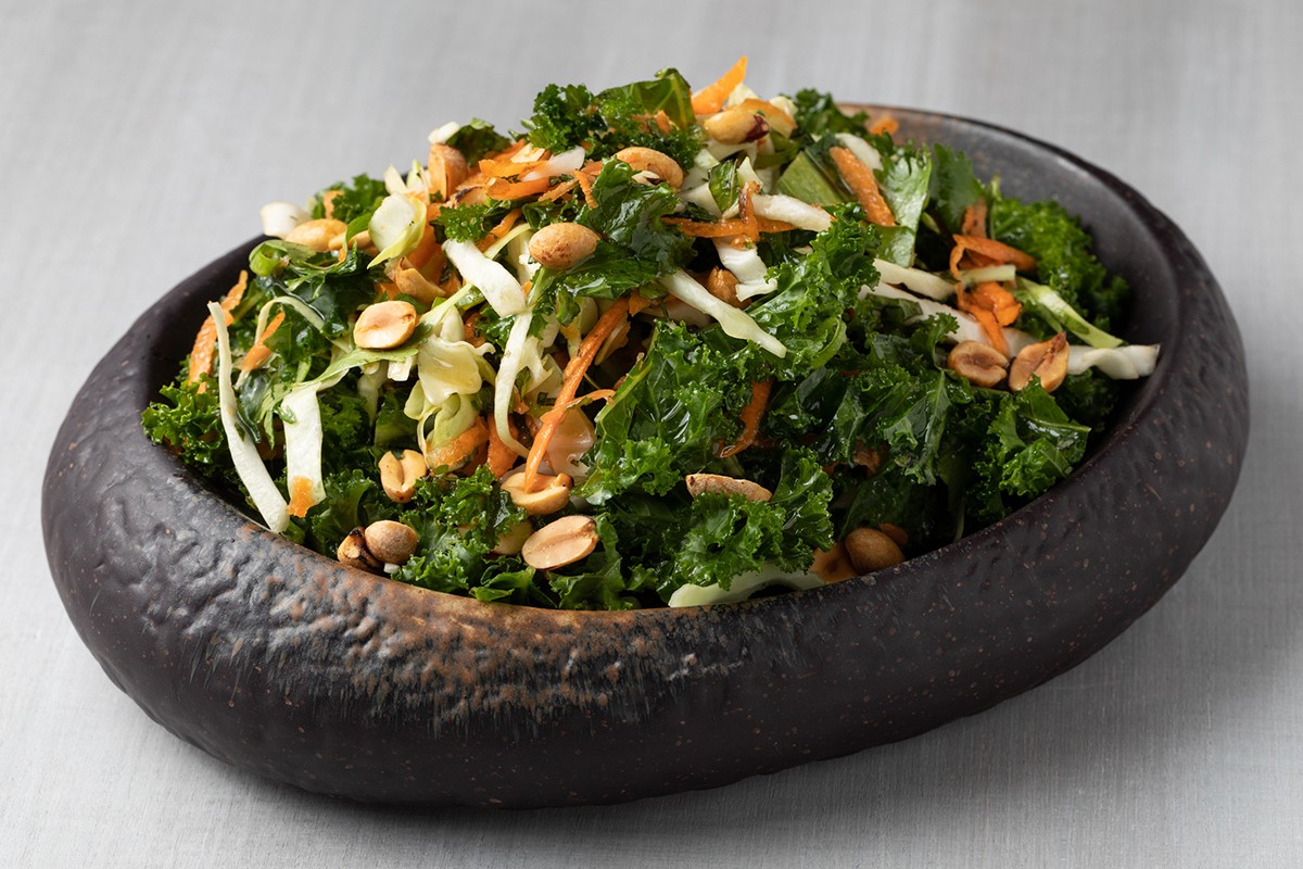 A bowl of kale salad with carrots and peanuts.