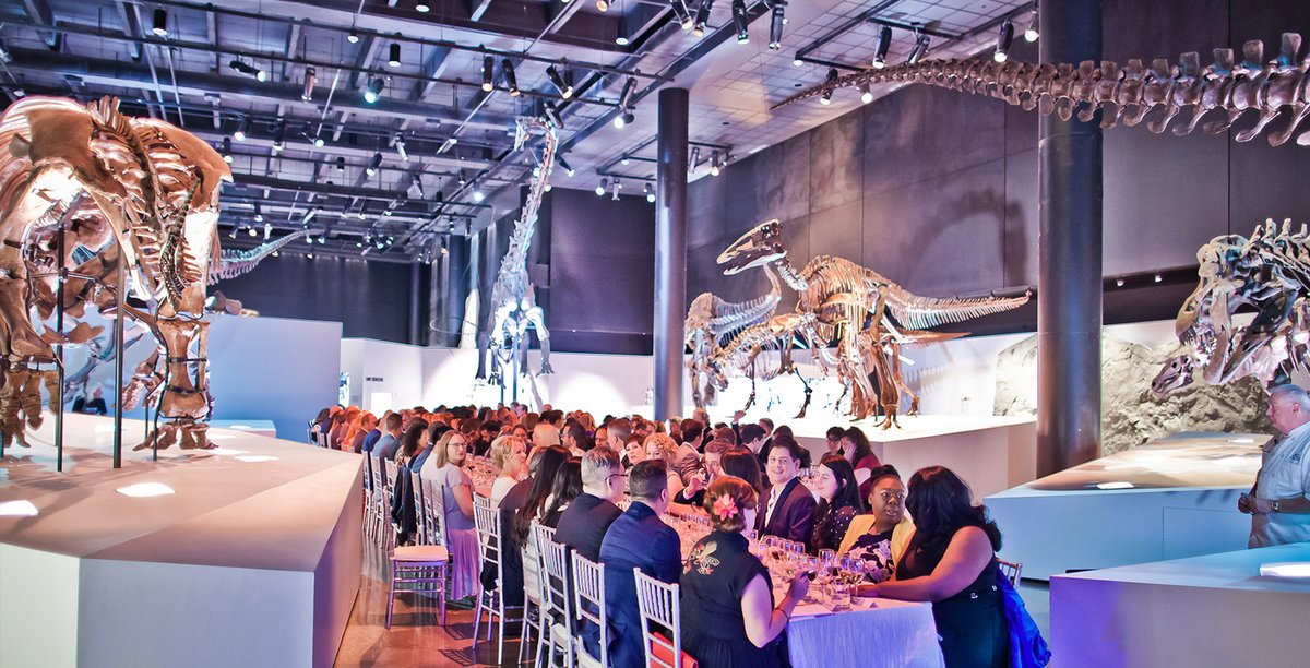 A group of people sitting at tables with dinosaurs on display
