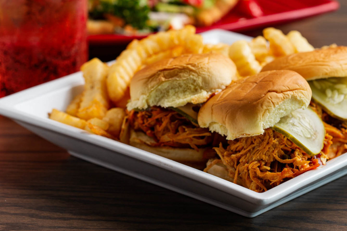 Bbq pulled pork sliders on a plate with fries and pickles.