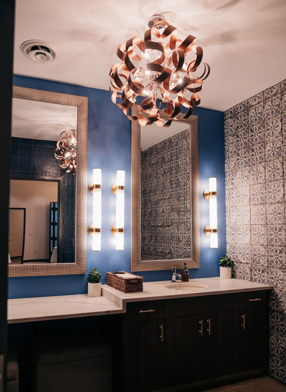 Elegant bathroom interior with decorative tiled walls, modern lighting, and dual vanity mirrors.
