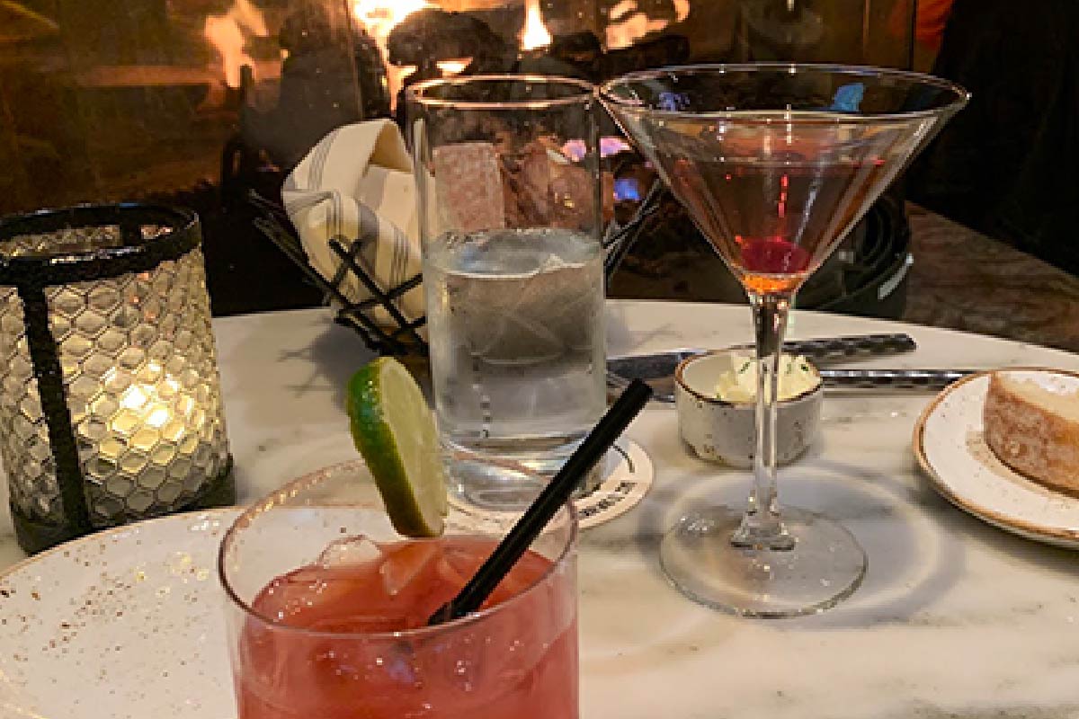Two drinks on a table in front of a fireplace.