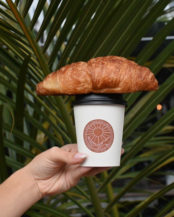 A person holding a croissant in a coffee cup