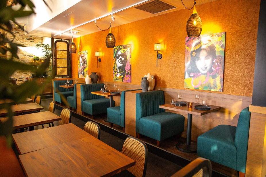Interior of a restaurant with teal booths, wooden tables, and vibrant art on the orange walls