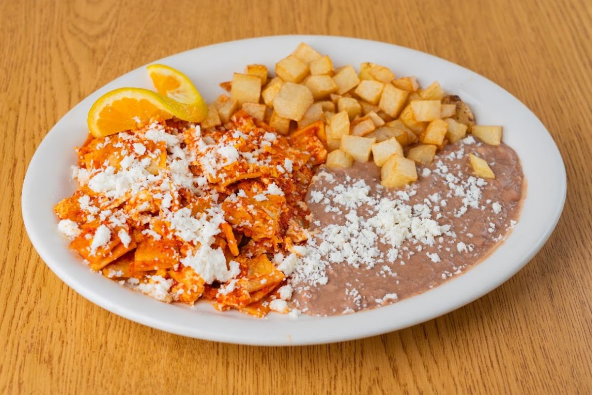 Chilaquiles, in red sauce, topped with cheese, served with rice, and potatoes