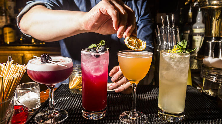 A hand places garnishes on four cocktails at a bar