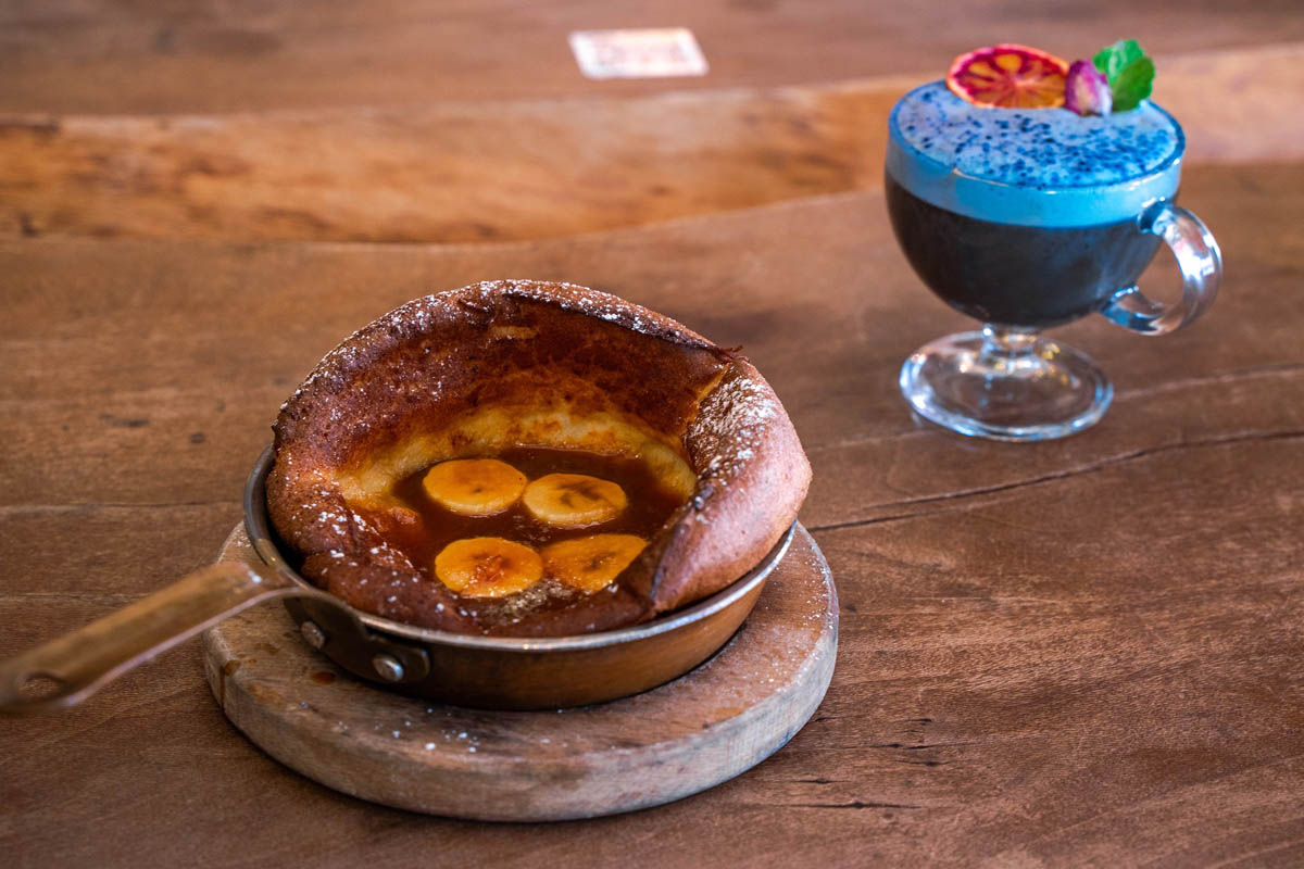 Banana Dutch Pancake pan served on the table with a glass of Peas of Mind cocktail