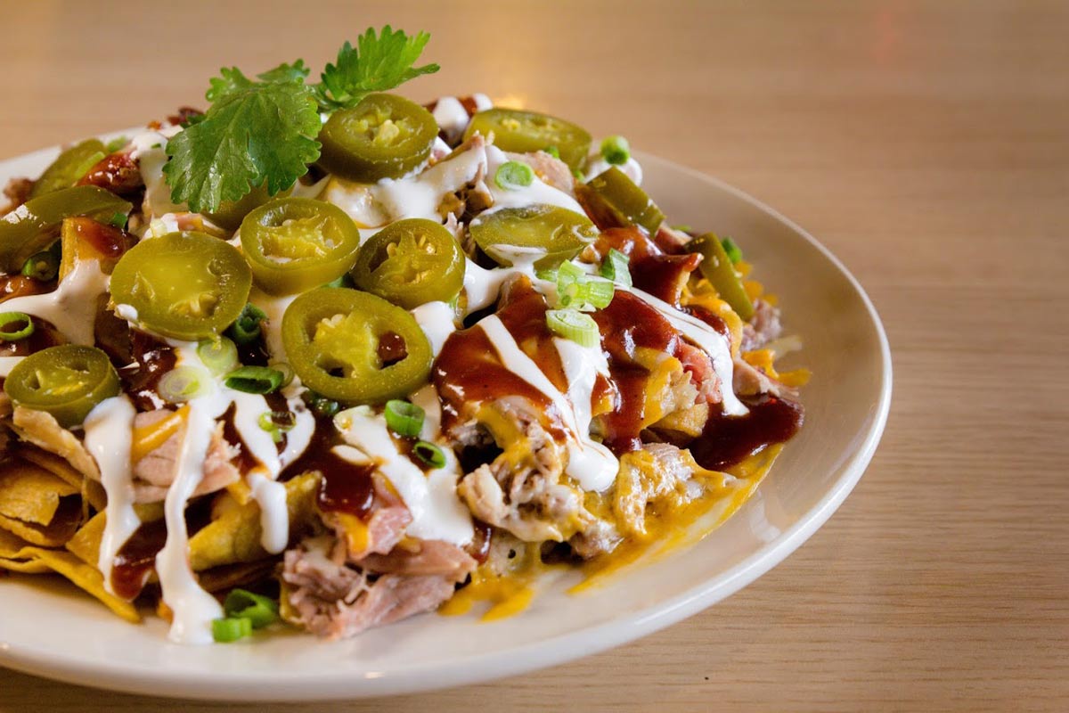 A plate of nachos topped with jalapeños, sour cream, and barbecue sauce